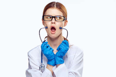 Young beautiful woman in glasses and in medical robe holds a stethoscope on white isolated backgroundの写真素材
