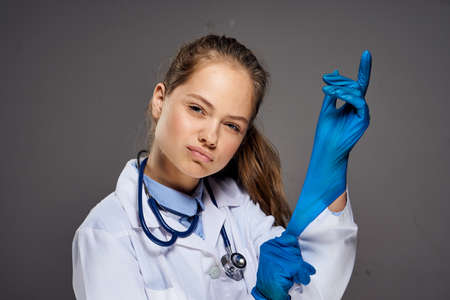 Young beautiful woman in medical robe puts on gloves on black background, doctor, medicine.の写真素材