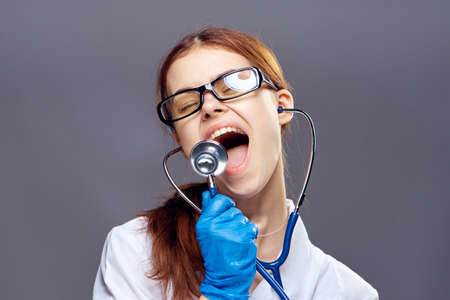 Young beautiful woman on a black background in medical clothes holds a stethoscope, emotions, doctor, medicine.の写真素材