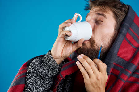 Man with a beard on a blue background drinking tea, illness, sick, cold.の写真素材