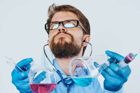 A man with a beard at a table on a light background holds laboratory utensils, scientist, science.の写真素材