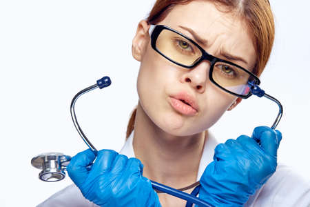 Beautiful young woman on white isolated background in glasses and in medical dressing gown holds a stethoscope, portrait.の写真素材