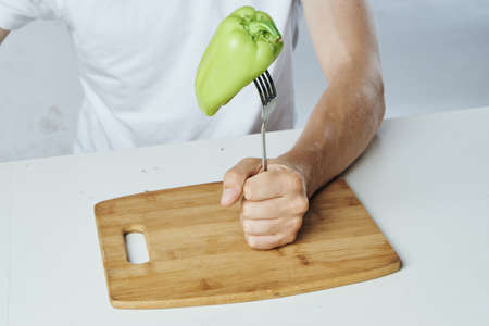 Man at the table holding fresh pepper on the fork, cutting board.