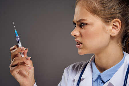 Young beautiful woman in medical dressing gown holds a syringe, portrait, doctor.の写真素材