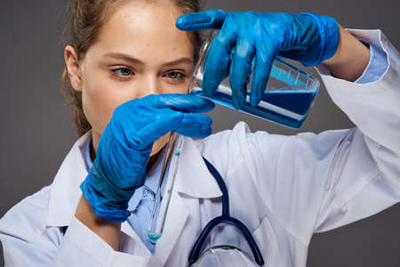 Young beautiful woman holds experiments in medical dressing gown on dark gray background.の写真素材