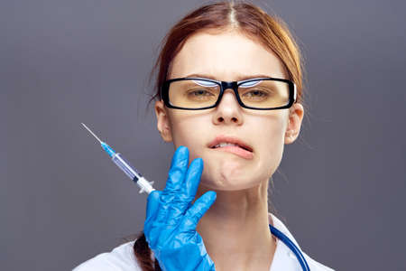 Young beautiful in glasses and in medical clothes holds a syringe on a dark gray background, portrait.の写真素材
