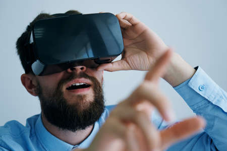 A man with a beard plays on a light background in glasses of virtual reality, entertainment.