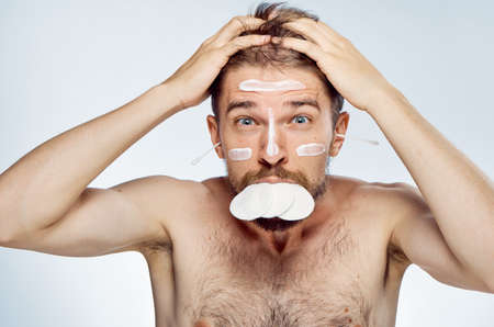 Man with a beard on a light background, cosmetic cream, ear wand, cotton wool, portrait, emotion.の写真素材