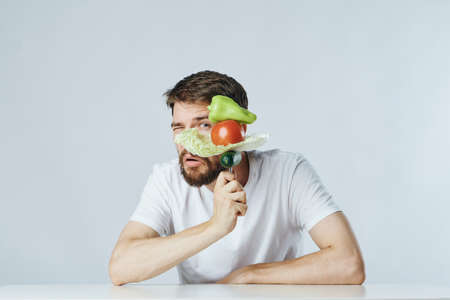 Man with a beard on a light background at a table holds vegetables on a fork, diet, vegetarian.の写真素材