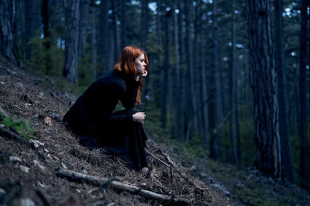 Woman in a black long dress is sitting in a dark forest.の写真素材