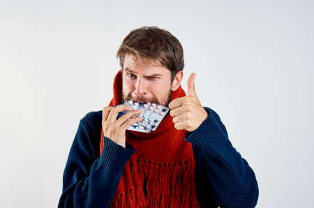 A man with a beard on a light background holds in his mouth a pack of pills.の写真素材