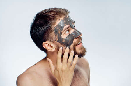 A man with a beard on a light background applies a cosmetic clay mask for the face, a portrait.の写真素材