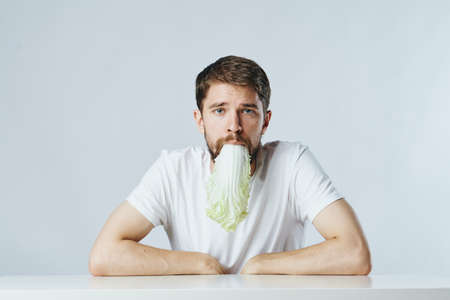 Man with a beard on a light background at the table holds a salad in his mouth, diet, vegetarianism, vegetables.の写真素材