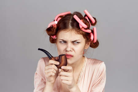 Woman housewife in curlers holds a smoking pipe on a gray background, portrait.の写真素材