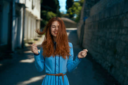 Beautiful woman in blue dress and with red hair in an alley in the city.