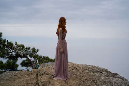 Beautiful woman in a long pink dress is standing on a cliff of a mountain, nature.