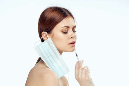 Beautiful woman on white isolated background holds a syringe, portrait, medical mask, plastic surgery, medicine.の写真素材