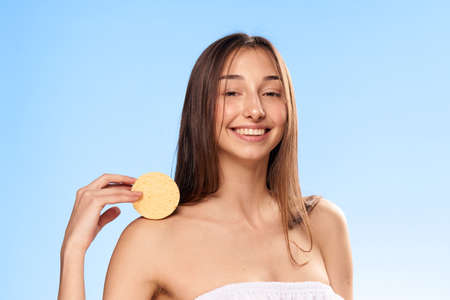Beautiful woman on a light blue background holds a sponge for make-up removal, portrait, smile.の写真素材