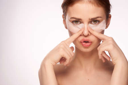 Beautiful woman on a light background in white patches for the eyes, facial treatment, portrait, empty space for copy.の写真素材