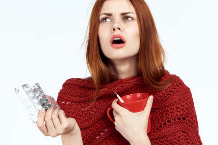 Beautiful woman on white isolated background holds a mug and pills, illness, sick, flu, portrait, emotions.の写真素材