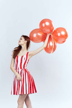 Beautiful young woman on a light background holds balloons in a striped red dress, smile.の写真素材