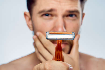 Man with a beard on a light background holds a razor, portrait.の写真素材