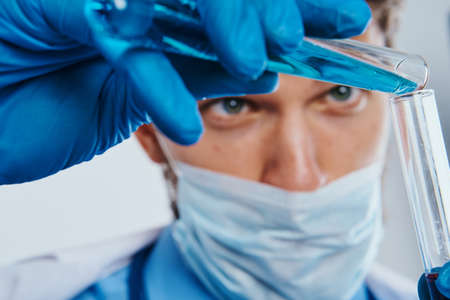 Man with a beard on a white background holds test tubes with multi-colored liquids, portrait,...