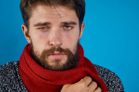 Man with a beard on a blue background in a scarf, portrait, emotion, patient, flu, illness, empty space for copy.の写真素材