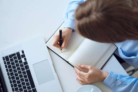 Young woman writes in a notebook at the desk in the office, business.