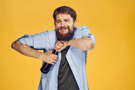 Man with a beard on a yellow background opens a bottle of beer, alcohol, emotions.