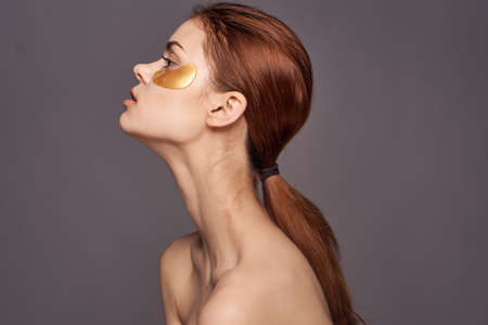 Young woman on a dark gray background in gold patches for the eyes, facial skin treatment, portrait,...
