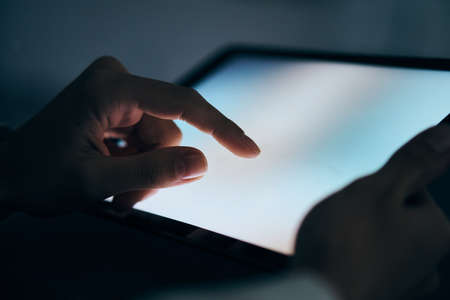 Hands, tablet, close-up, darkness.