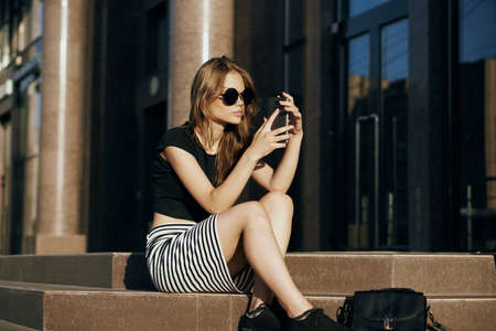 Woman in sunglasses is holding a phone on the street.の写真素材