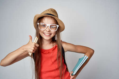 little girl wearing glasses and wearing a hat on gray background smiling.
