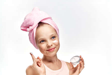 little girl puts cosmetic face cream on white isolated background.の写真素材