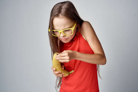 Girl in yellow glasses cleans a banana, portrait.の写真素材