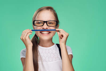 little girl with glasses holds a pen and smiles, portrait.の写真素材