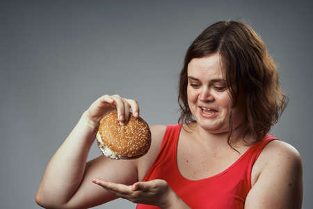 fat woman holding a hamburger and laughing, fast food.の写真素材