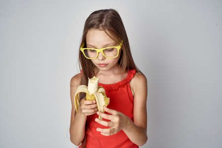 a little girl in yellow glasses cleans a banana.の写真素材