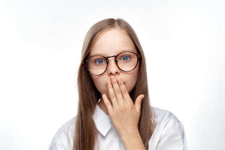 little girl with glasses covers her mouth with her hand, emotions, portrait.の写真素材