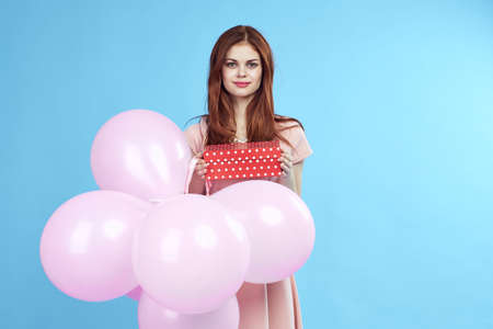 a woman with red hair is holding a box and pink balloons.の写真素材