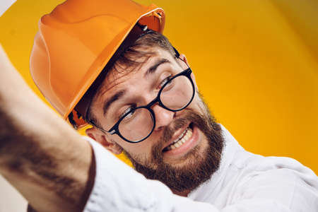 man with a beard engineer in glasses and wearing a helmet on a yellow background, portrait, emotion.