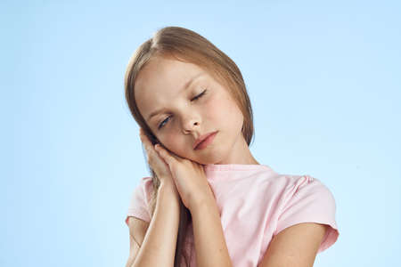 cute little girl with closed eyes holding hands near face on blue background portrait.の写真素材