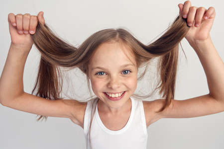 cheerful little girl smiling holding her hands her hair on a light background portrait.の写真素材