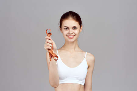 sports positive girl squeezes a measuring tape in her hand against a light background.の写真素材