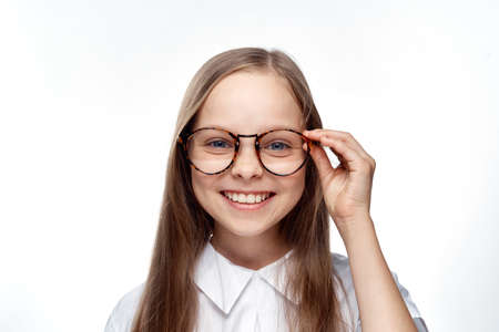 little cute little girl smiles and straightens glasses on white isolated background.の写真素材
