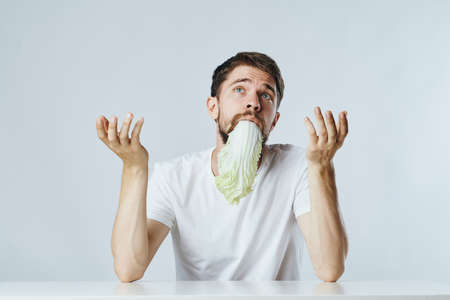a man with a beard at the table holds a leaf of lettuce in his mouth.
