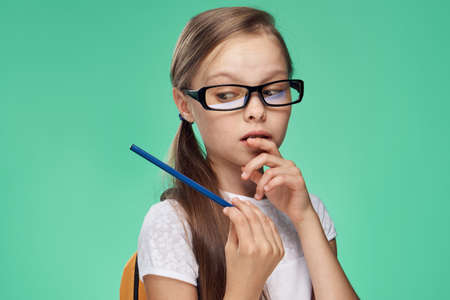 a schoolgirl in glasses holds a pen on a green background.