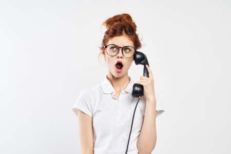emotions on face, young woman in glasses talking on stationary phone on light background.の写真素材