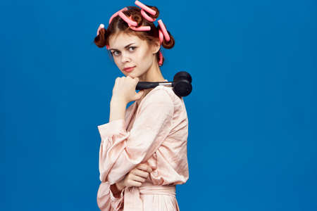 housewife with curlers on her head in her hand a hammer for beating meat on a blue background.の写真素材